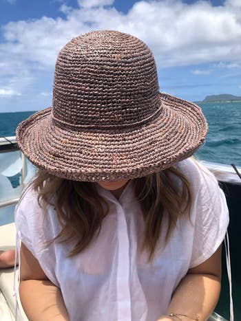 Person sitting on a boat, wearing a straw hat, reading a book. Ocean and sky visible in the background