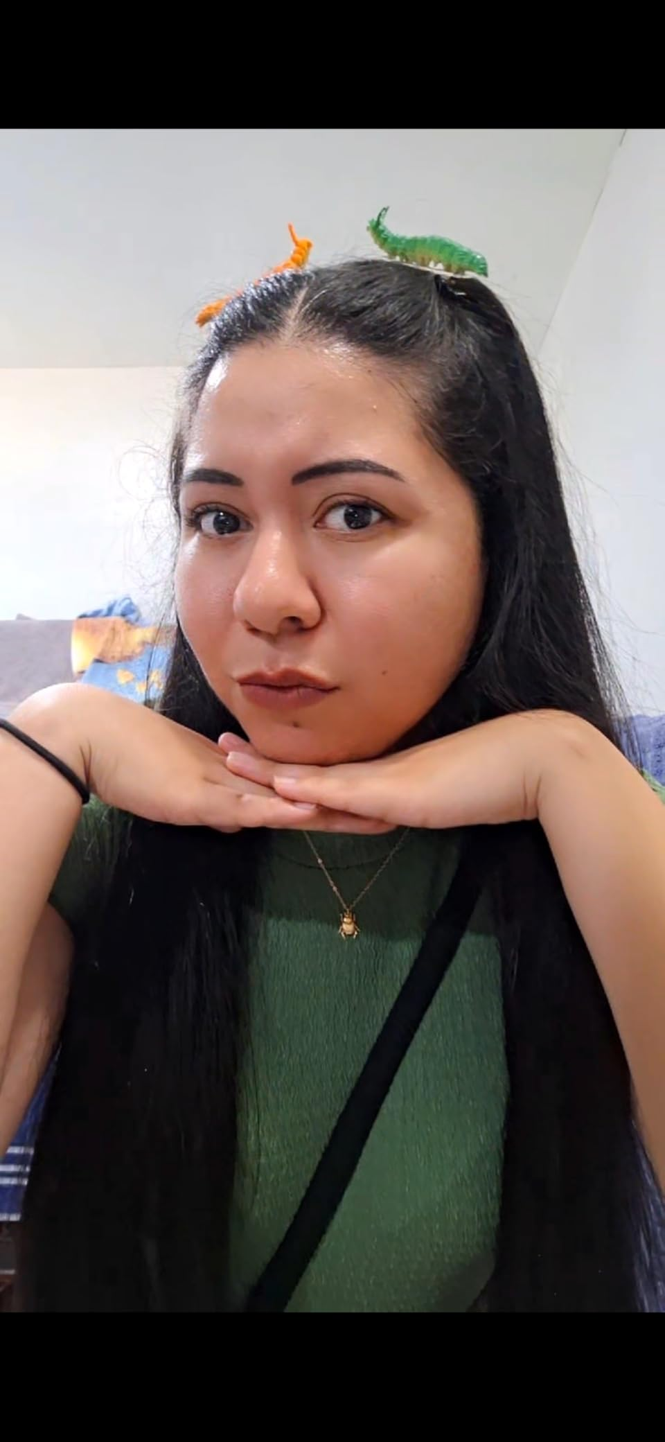 Person with agelong  hairsbreadth  wearing a greenish  top, accessorized with dinosaur hairsbreadth  clips, resting their chin connected  their hands successful  a playful pose