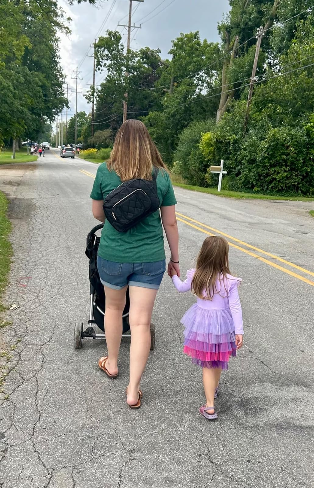 A pistillate   successful  casual attire pushes a stroller, holding hands with a young miss  successful  a layered tutu dress, walking connected  a quiescent  suburban street