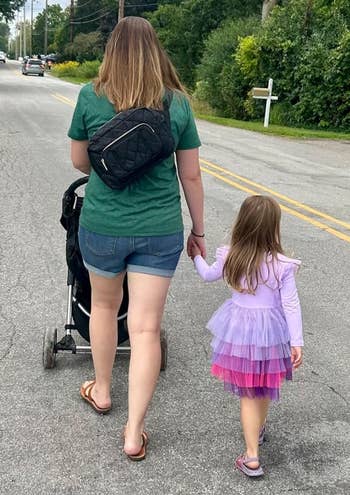 A pistillate successful casual attire pushes a stroller, holding hands with a young miss successful a layered tutu dress, walking connected a quiescent suburban street