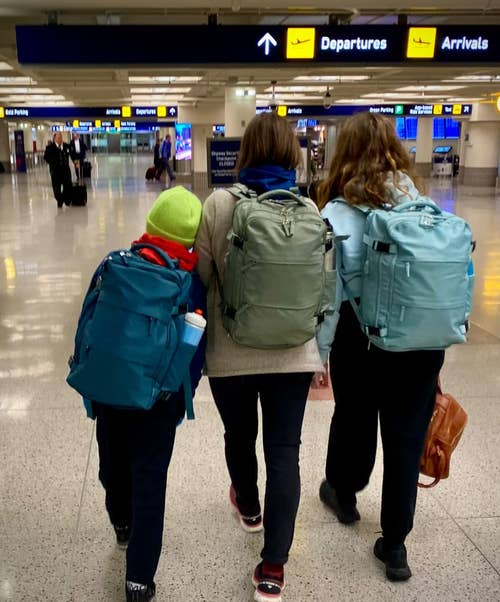 reviewer photo of three people walking through the airport all wearing the travel backpack