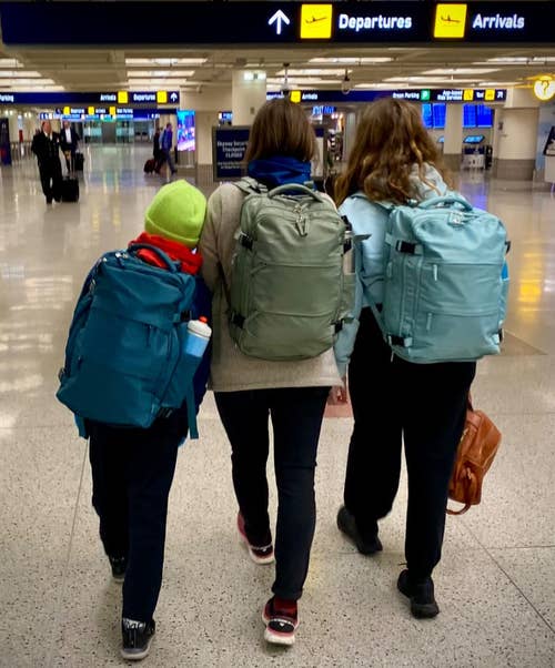 reviewer photo of three people walking through the airport all wearing the travel backpack