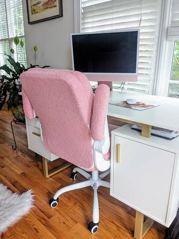 A stylish ergonomic office chair with a plush texture sits at a modern desk with a computer monitor and decorative plants nearby