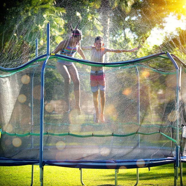 two kids jumping on the trampoline with the water hoses hooked up