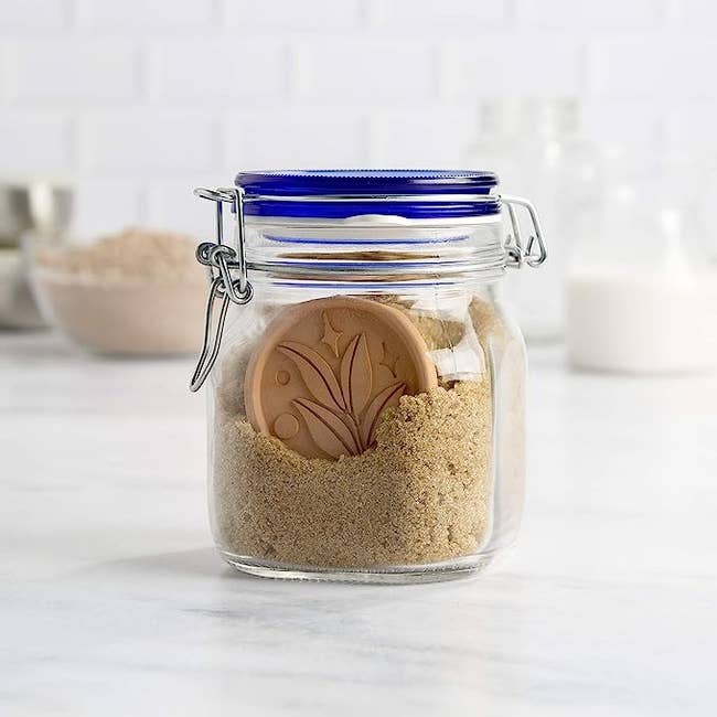 Sealed glass jar on a kitchen counter containing brown sugar and a terracotta disc to maintain freshness
