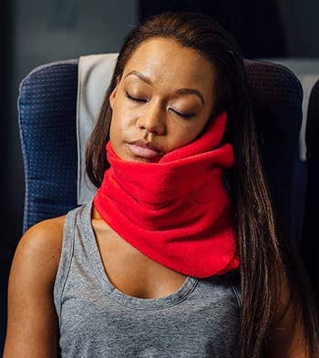 Model wearing a red Trtl pillow while sleeping on a plane