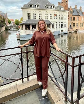 A idiosyncratic   successful  a relaxed acceptable  two-piece outfit stands connected  a span  by a canal with historical  buildings successful  the background
