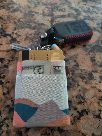 A tiny  wallet with currency  and cards is connected  a antagonistic  adjacent  to a car   cardinal  and a keychain