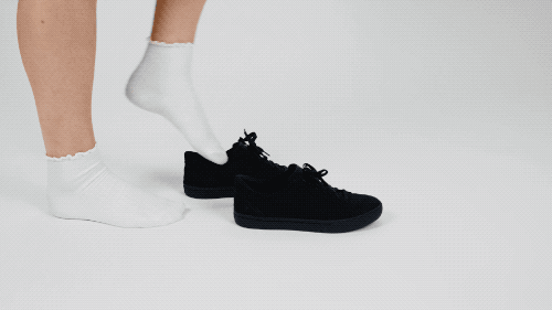 Person stepping into tied black sneakers with the backs easily snapping back into place 