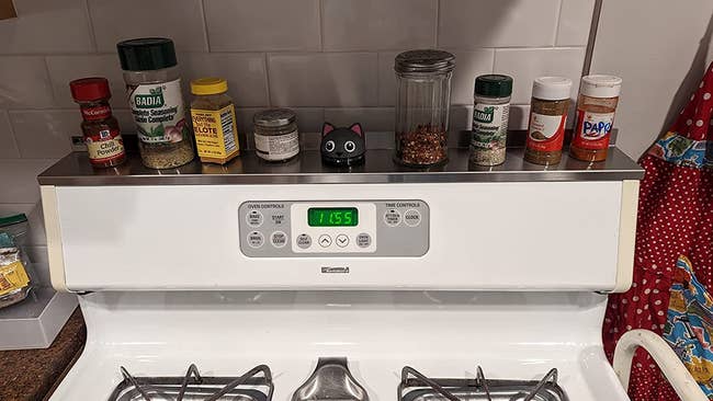 A magnetic shelf on top of a stove with spices and other objects on top