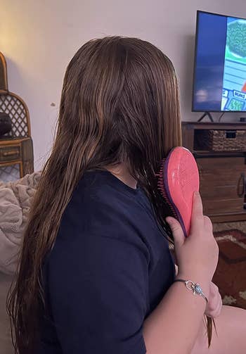 Reviewer brushing their long hair with a pink brush 