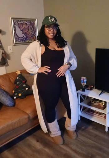 Person successful  a cozy surviving  country   wearing a long, airy  cardigan implicit    a achromatic  outfit, UGGs, and a greenish  LA cap, posing confidently