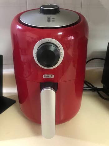 Compact red air fryer with a dial timer on a kitchen counter