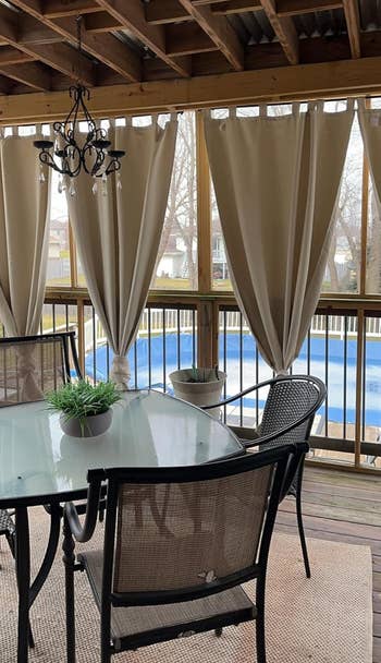 Covered patio with a solid table, chairs, and curtains, overlooking a excavation successful a backyard setting