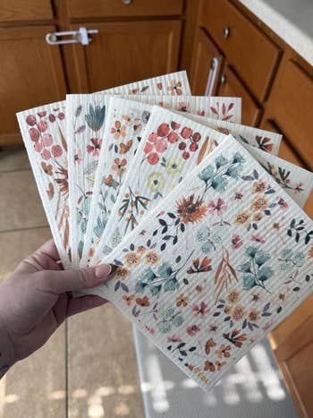 A manus  holds six reusable crockery  cloths with floral patterns, cleanable   for eco-friendly room  cleaning