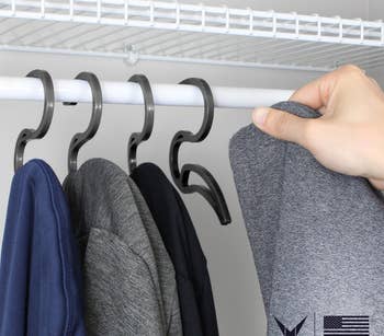 four black hoodie hangers in closet with person's hand removing one