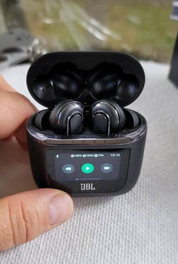 reviewer's open ear bud case with screen on front showing play or fast forward