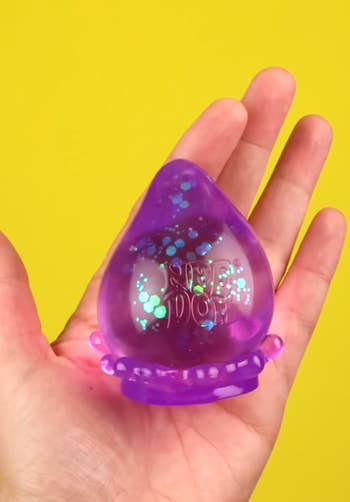 Hand holding a translucent purple slime toy with small bubbles inside, set against a yellow background