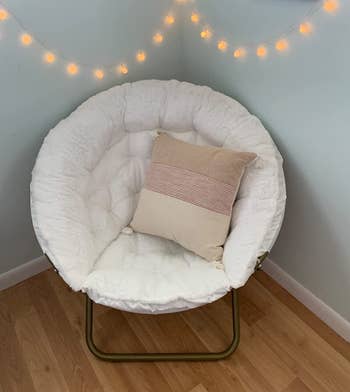 White saucer chair with metal curved foldable legs, faux fur tufted cushion, and pink and cream throw pillow