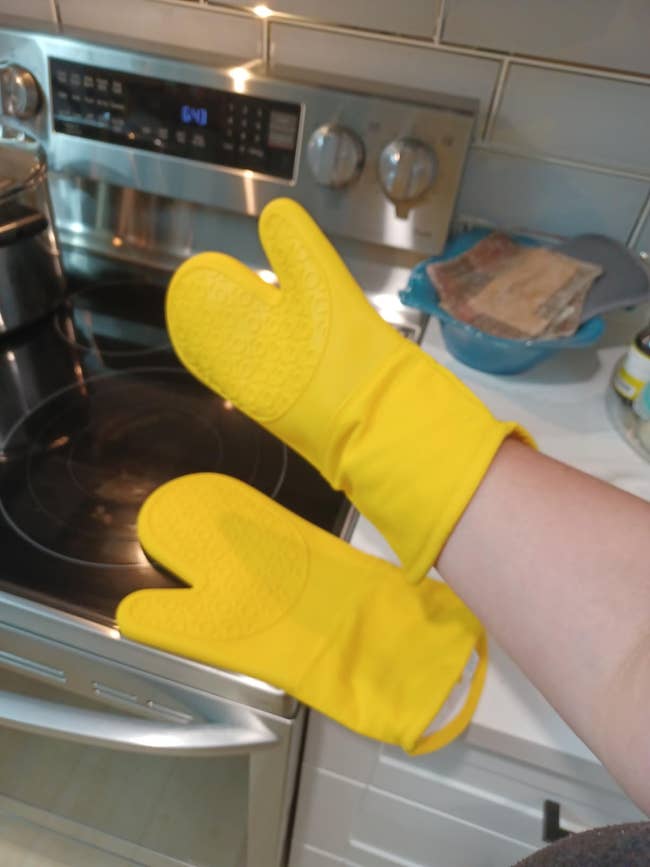 Person's manus wearing 2 yellowish oven mitts successful a room adjacent a stovetop, indicating usage for cooking oregon baking