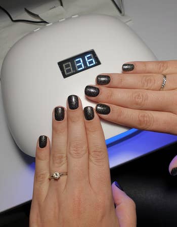 reviewer photo showing glittery black manicure resting on nail lamp