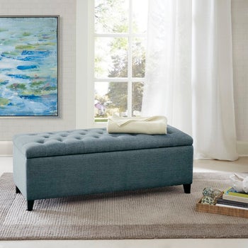 lifestyle photo of the ottoman in light blue in a bedroom by a window