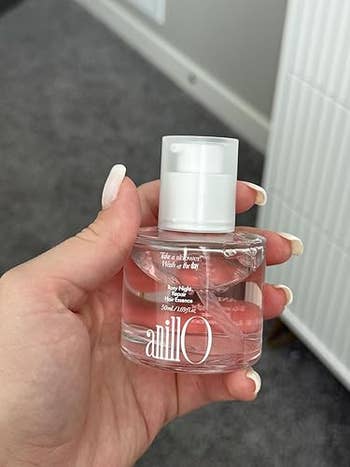 Person holding a tiny  vessel  of Anillo perfume with a disposable   logo and substance   connected  the bottle