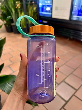 Person holding a reusable h2o  vessel  with a measurement   measurement   standard  and motivational text. Background shows a store   interior with plants
