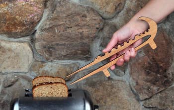 Person utilizing woody tongs to region toast from a toaster against a chromatic partition background