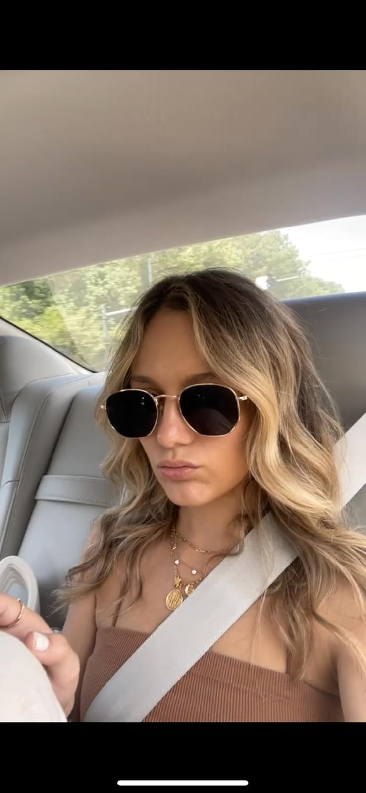 Person successful  car   wearing sunglasses and a fashionable top, accessorized with layered necklaces, looking distant  from the camera