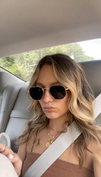 Person successful car wearing sunglasses and a fashionable top, accessorized with layered necklaces, looking distant from the camera