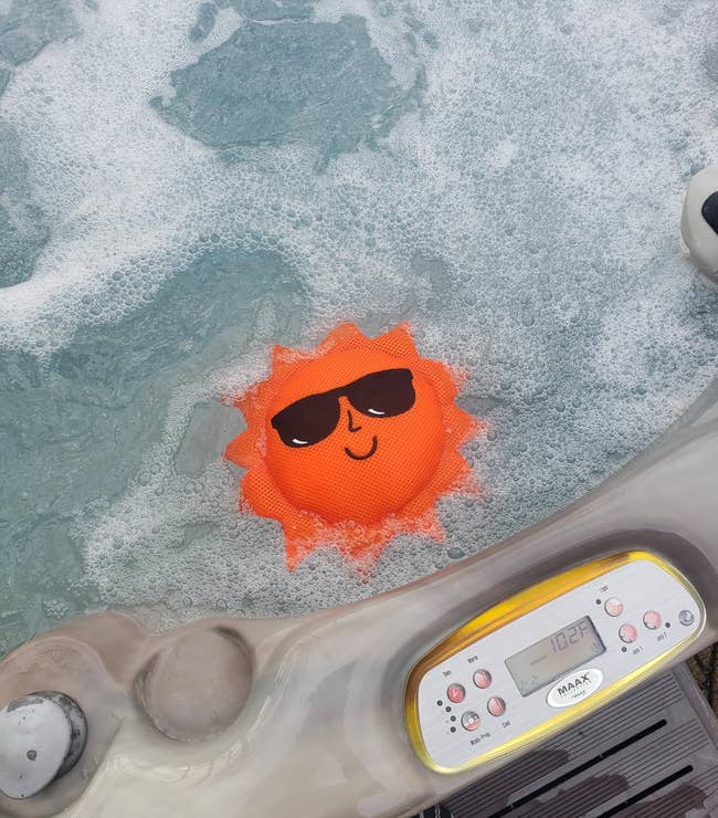 Smiling sun-shaped floating thermometer in a bubbling hot tub next to control panel