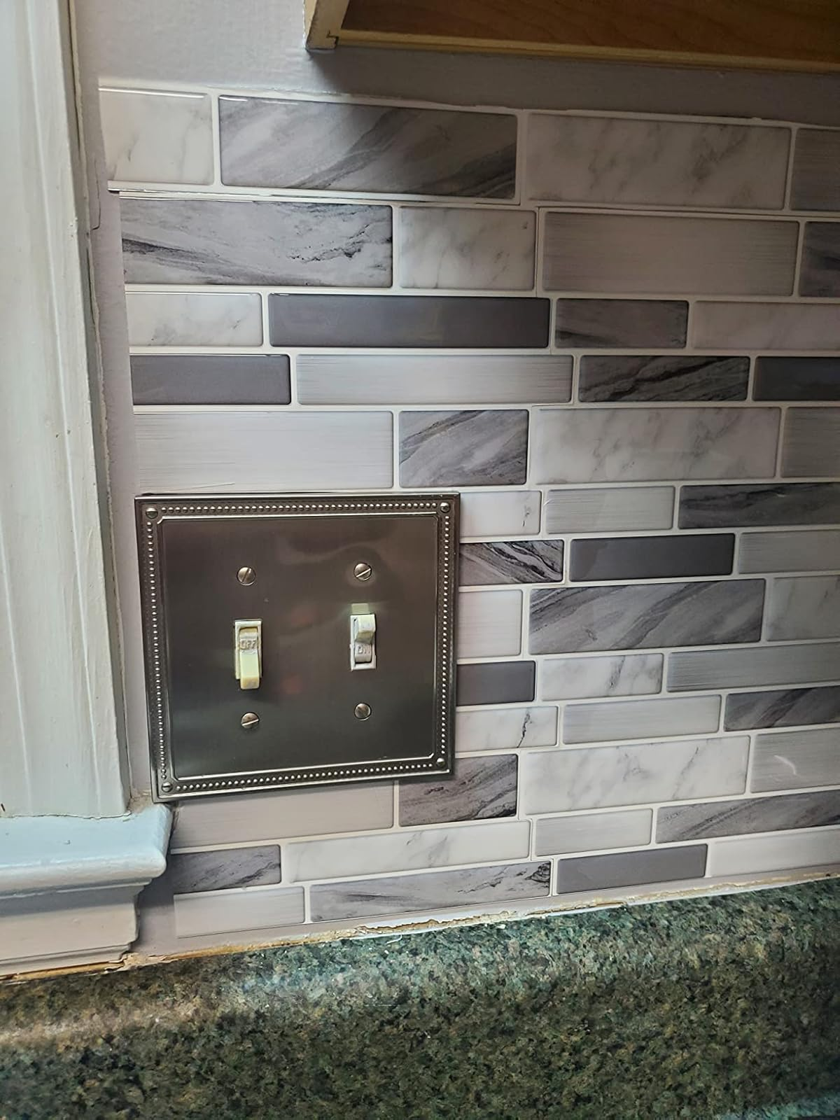 Backsplash ubin dekoratif dengan penutup sakelar lampu logam dalam pengaturan dapur, menampilkan desain modern dan penuh gaya