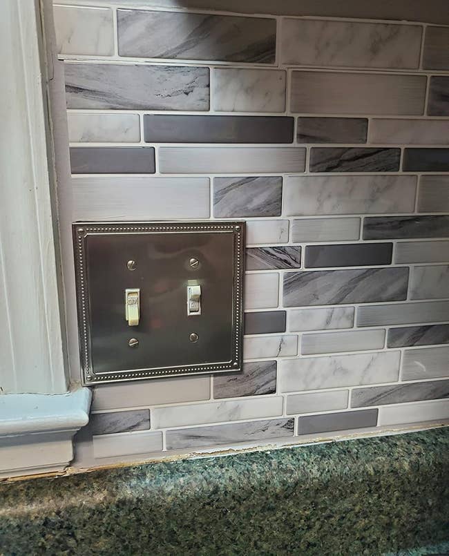 Backsplash ubin dekoratif dengan penutup sakelar lampu logam dalam pengaturan dapur, menampilkan desain modern dan penuh gaya