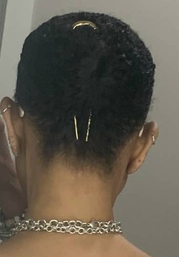 Reviewer with short hair styled with gold pins, wearing earrings and a chunky chain necklace, photographed from the back