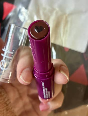 A person's manus  holds a lipstick with a bosom  imprint connected  the tip, adjacent  to a transparent cap