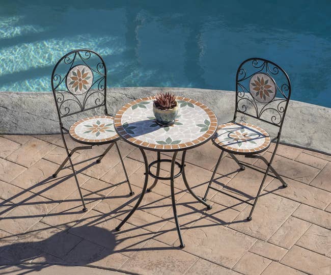 Black, orange, and green mosaic bistro chairs and round table next to a pool