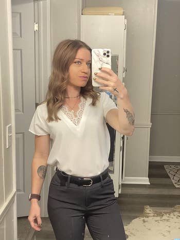 Person in a white top with lace detail taking a mirror selfie, styled with black belt and jeans