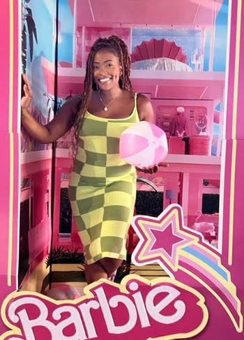 reviewer posing in a Barbie box wearing a sleeveless, checkered dress 