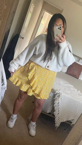 A idiosyncratic takes a reflector selfie wearing a textured top, a patterned skirt, and sneakers. Bedroom decor disposable successful the background
