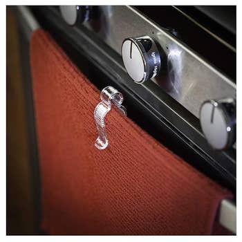 Transparent towel hook on an oven door with a red towel hanging from it