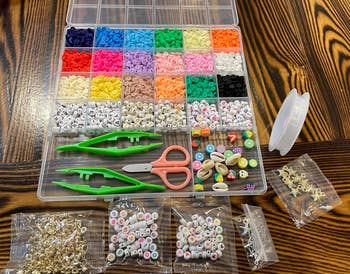 Assorted beads in a compartmentalized box with tweezers and scissors, plus packs of letters and charms 
