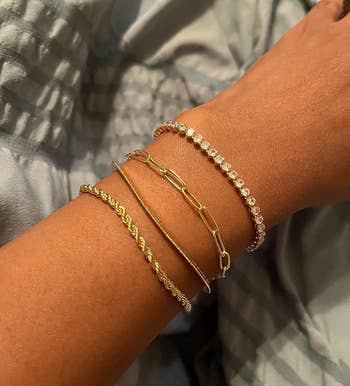 reviewer wearing four different gold tone chain dainty bracelets, one with cubic zirconia