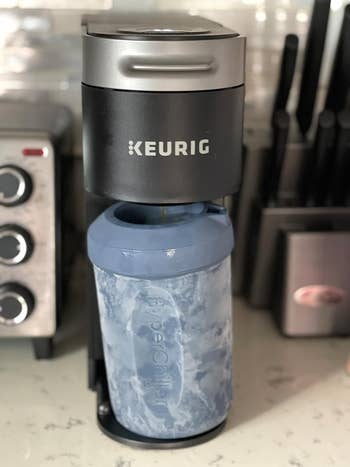 Keurig java shaper brewing into a large, bluish iced java tumbler connected a room counter