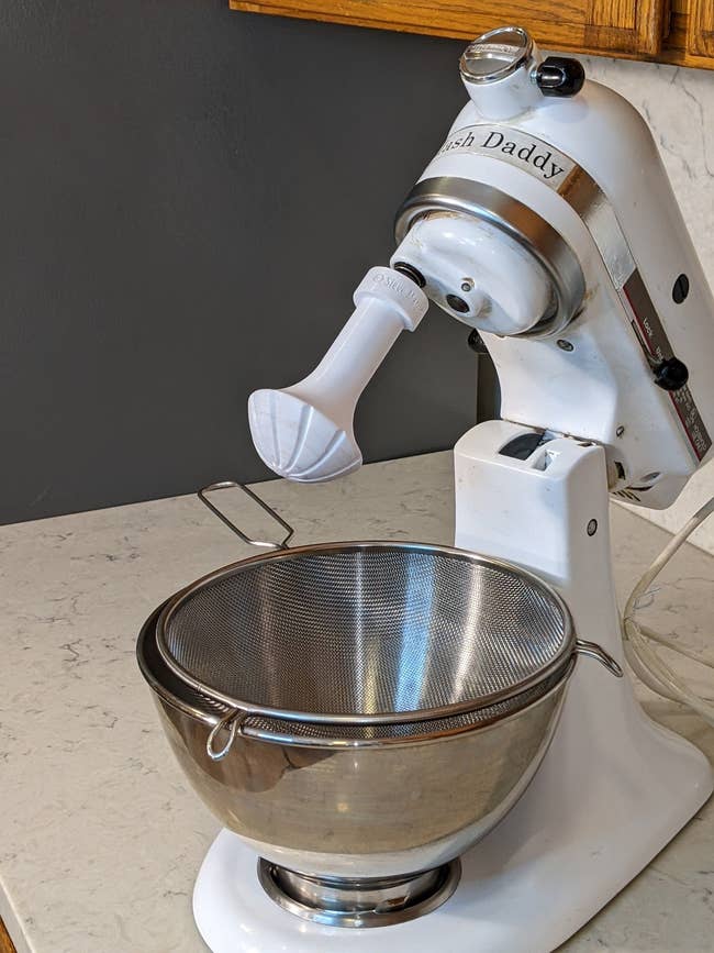 A stand mixer with a sifter attachment and a stainless steel bowl on a countertop
