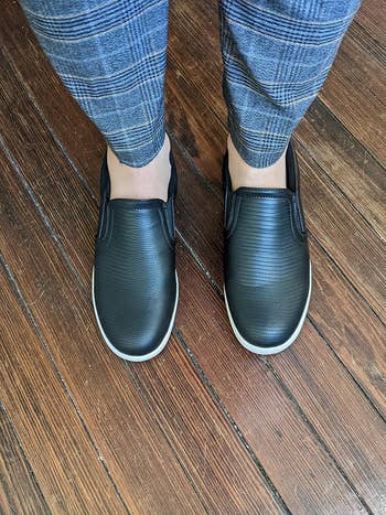 Person wearing achromatic textured slip-on shoes with plaid pants, lasting connected woody flooring