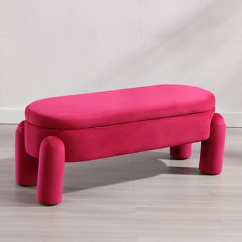A pink velvet bench with a curved seat and cylindrical legs