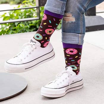 Person wearing white sneakers and donut-themed socks