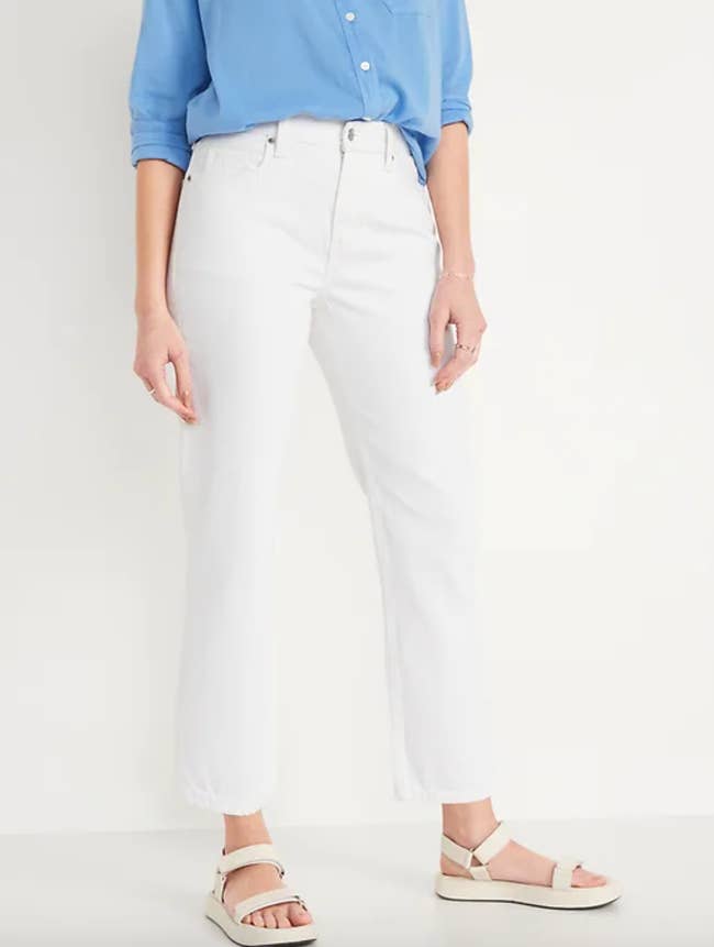 Model is wearing white denim jeans, cream colored sandals, and a blue button down