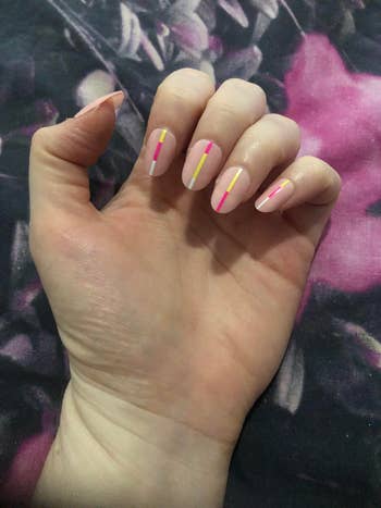 writer's hand with oval shaped light pink fake nails with neon stripes down the middle